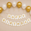 Gold and white happy birthday decoration with metallic balloons, ribbon curls and elegant birthday banner for party setup.
