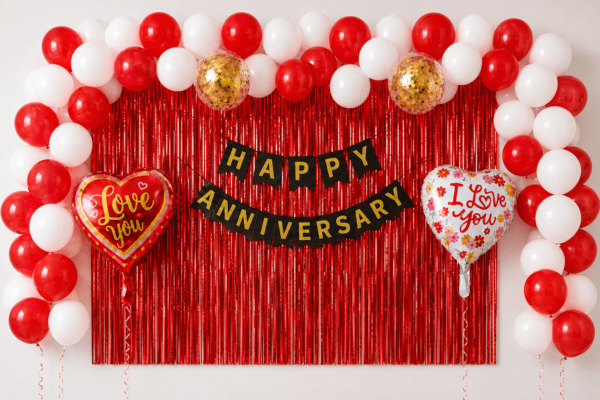 Happy Anniversary Red & White Balloon Decoration with Red Foil Curtain Red and white anniversary balloon decoration with red foil curtain backdrop, black gold Happy Anniversary banner, love you heart foil balloons and gold confetti balloons.