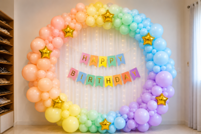 Pastel rainbow birthday decoration with balloon arch, gold star foil balloons, fairy light curtain and happy birthday banner.