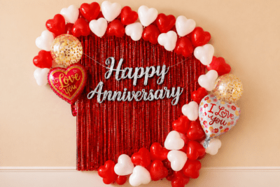 Happy Anniversary Red Heart Balloon Decoration Setup Red and white heart balloon anniversary decoration with red foil curtain, silver Happy Anniversary banner, love you foil balloons and golden confetti balloons.