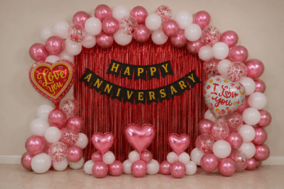Romantic Happy Anniversary Decoration with Pink & White Balloons and Red Foil Curtain Romantic happy anniversary decoration with red foil curtain backdrop, black and gold cardstock banner, metallic pink and white balloon arch, red confetti balloons, pink heart balloons and love you foil balloons for anniversary celebration.